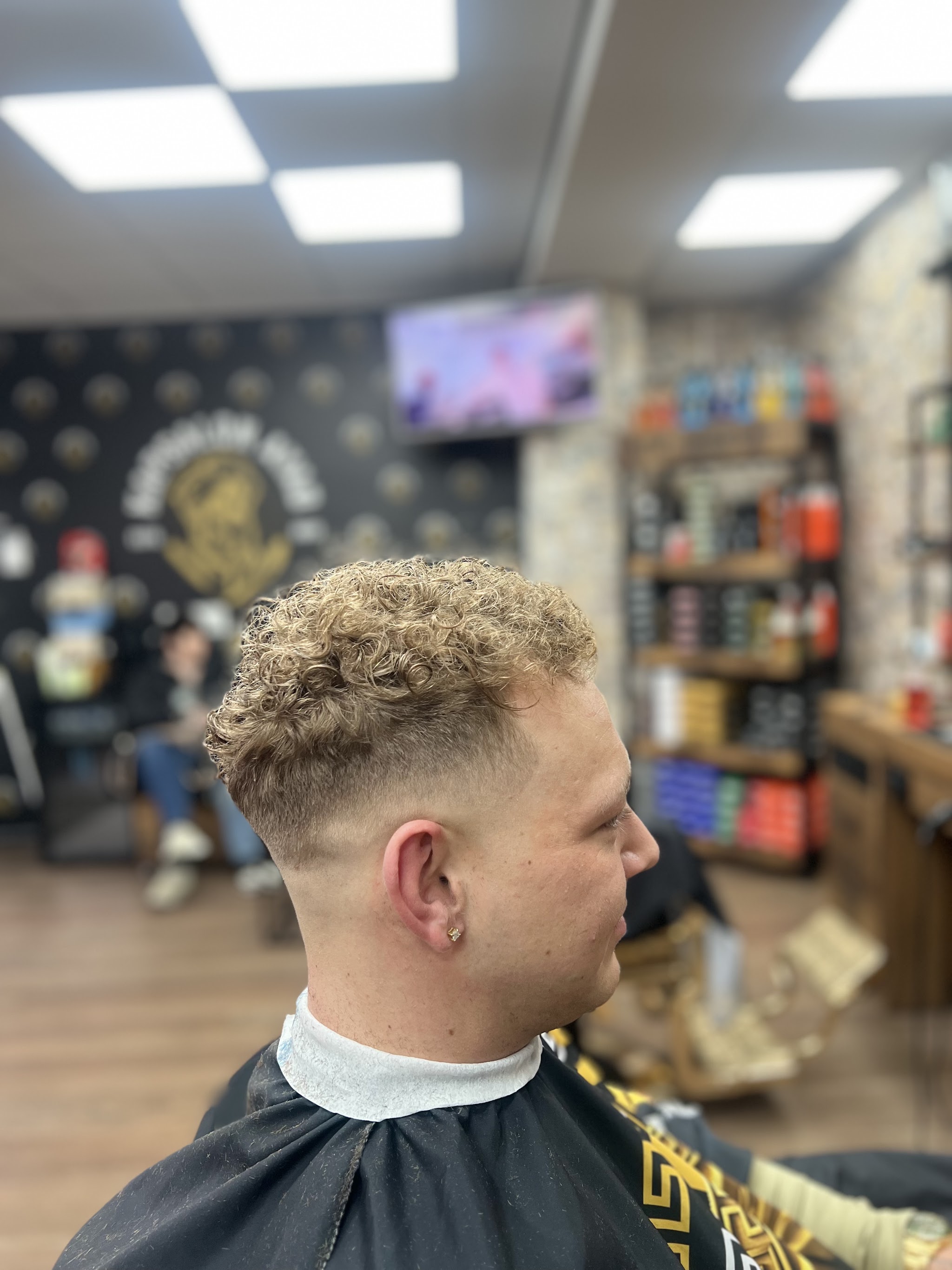 Krullen bovenop en een strakke fade aan de zijkant, voor de zwarte muur met het gouden logo